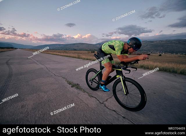 triathlon athlete riding professional racing bike on morning workout sunset or sunrise in background