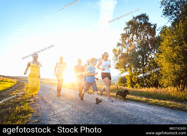 Playful family running and playing on a path in backlit summer landscape
