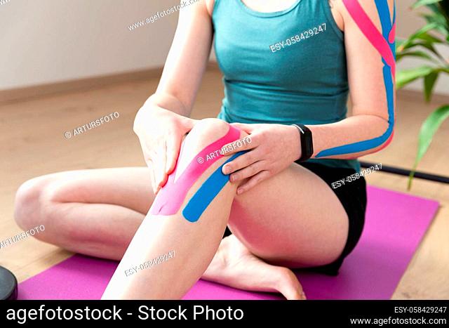 Kinesiotaping, kinesiology. Female athlete with kinesiotape, muscle tape on knee. Wourkout at home