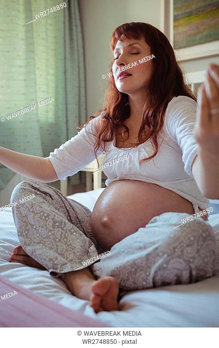 Pregnant woman performing yoga on bed