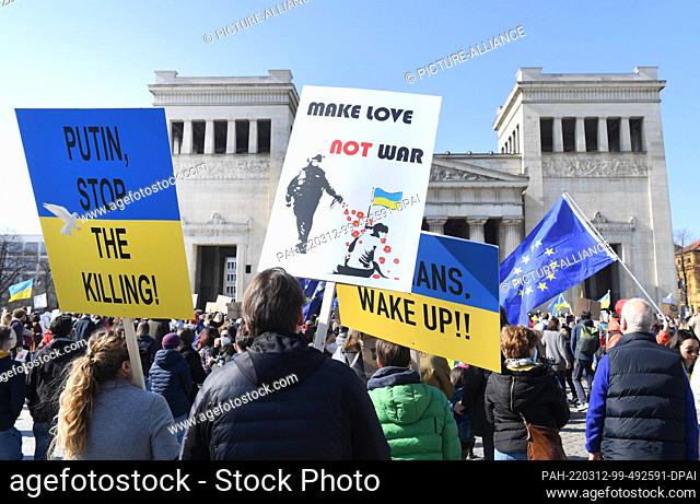 12 March 2022, Bavaria, Munich: Participants of a rally against the war in Ukraine demonstrate on Königsplatz with placards reading ""Make Love - Not War"" and...