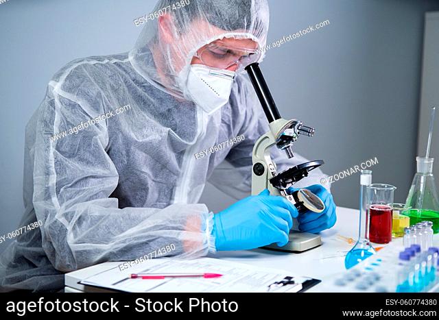 Scientist examining sample with a microscope, doing medical research in science laboratory. Male laboratory assistant in protective clothing studying new...