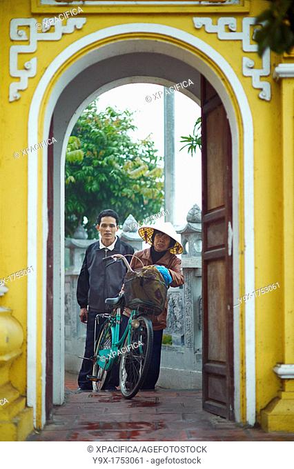 A man and an old woman with a bicycle pearing through an ornate archway at The Tran Quoc Pagoda