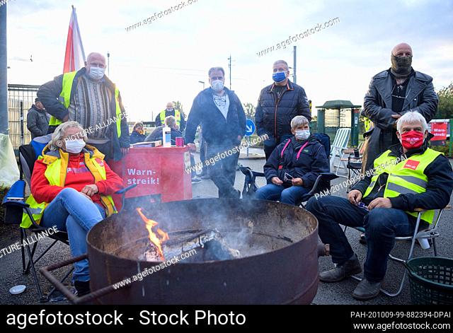 09 October 2020, Brandenburg, Brandenburg/Havel: Strikers stand and sit at a fire bowl in front of the entrance to the Brandenburg an der Havel GmbH transport...