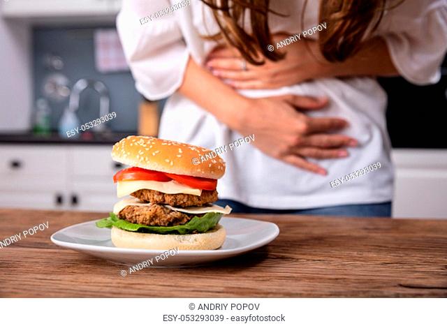 Mid-section Of Woman Suffering From Stomach Pain While Having Burger