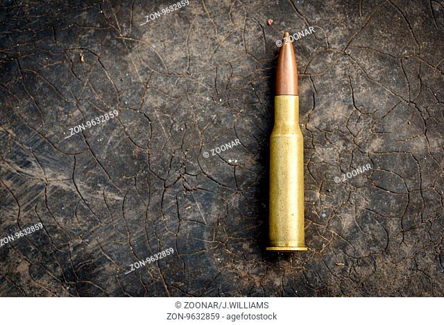 Single 7.62mm bullet with brass shell casing. Unfired ammunition for modern assault rifles like the AK-47 Kalashnikov on a black cracked rubber background