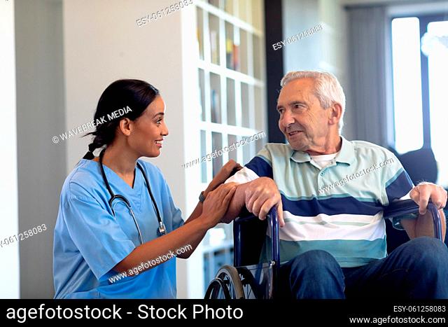 Smiling biracial female physiotherapist talking with caucasian senior man sitting on wheelchair
