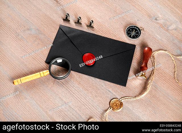 Blank black vintage envelope, sealing wax, magnifier, stamp, compass and stamp on wooden background. Responsive design mock up. Postal stationery