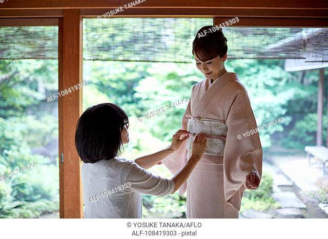 Young Japanese woman putting on traditional kimono