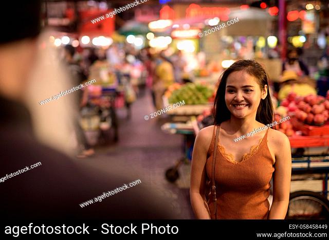 Portrait of mature bearded tourist man asking directions from young Asian woman around Chinatown in Bangkok city at night