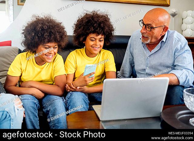 Grandfather talking to grandsons watching laptop at home