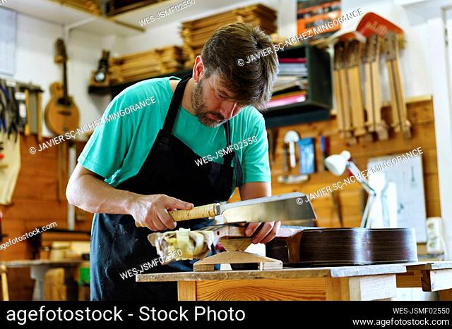 Luthier cutting fretboard on workbench in workshop
