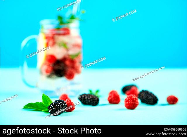 Fresh berries cocktail in glass jar. Fresh summer cocktail with mix of berries, lemon and mint on blue background. Party, drink, summer concept