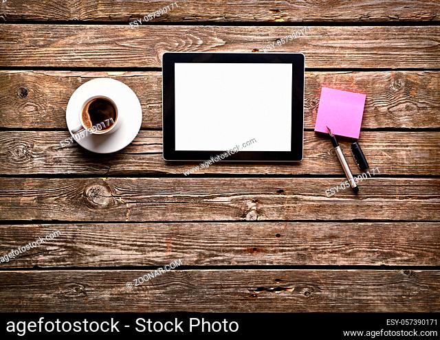 Digital tablet computer with sticky note paper and cup of coffee on old wooden desk. Simple workspace or coffee break with web surfing