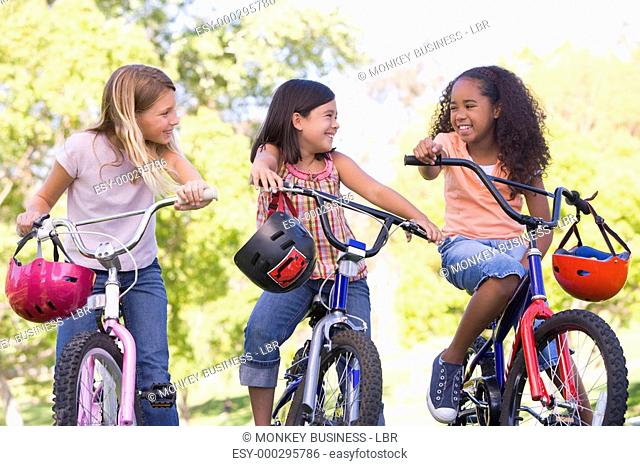 Three young girl friends outdoors on bicycles smiling