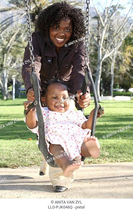 Mother swinging her daughter on the swing in the park. Dewaal Park, Cape Town, Western Cape Province, South Africa