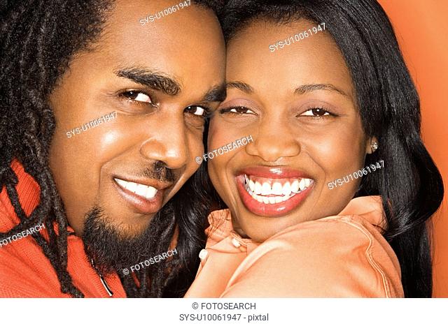 Smiling African-American mid-adult couple wearing orange clothing on orange background