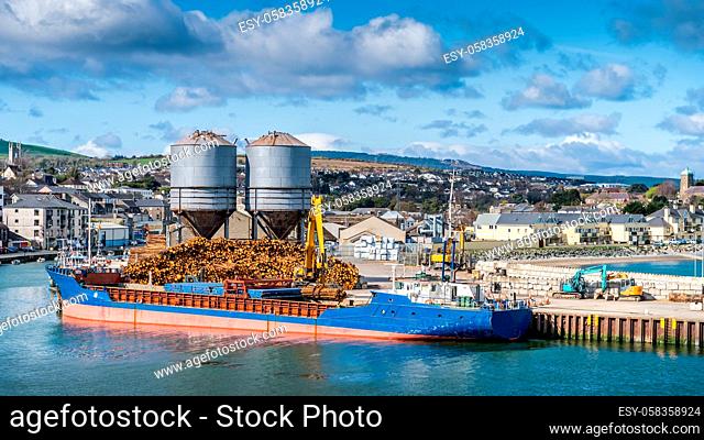 Crane with wood logs gripple loading timber on cargo ship for export in Wicklow commercial port. Transport industry in Ireland