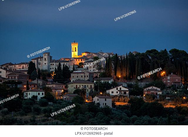 Twilight view of medieval hilltop town of MonteCastello di Vibio. stone houses and belltower, olive groves on slope below, with pink and blue twilight sky