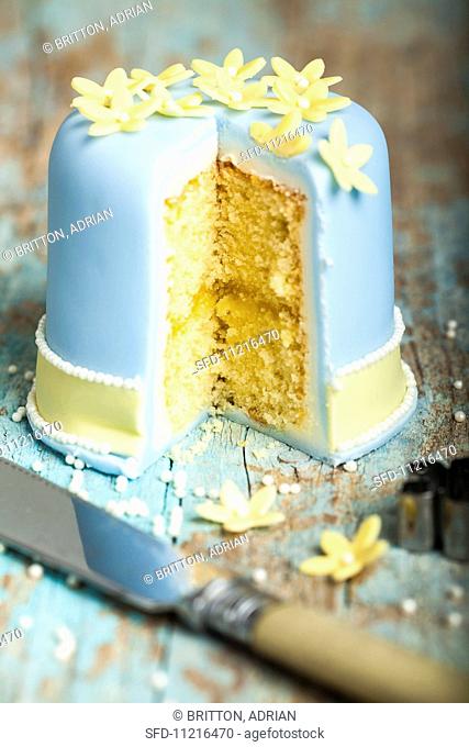 A layer cake iced with blue fondant and decorated with marzipan flowers, cut open to show the centre