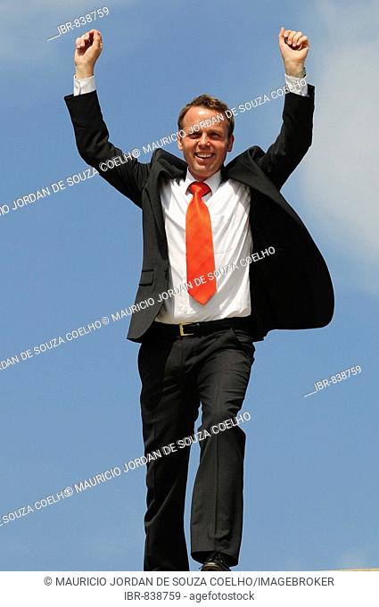 Businessman wearing a suit with a red tie, raising his arms in the air and celebrating, success, victory, delight
