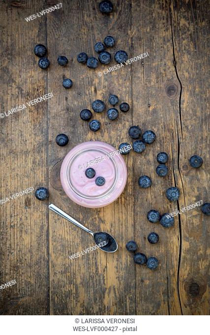 Blueberries (Vaccinium myrtillus), spoon and glass of blueberry yoghurt on wooden table