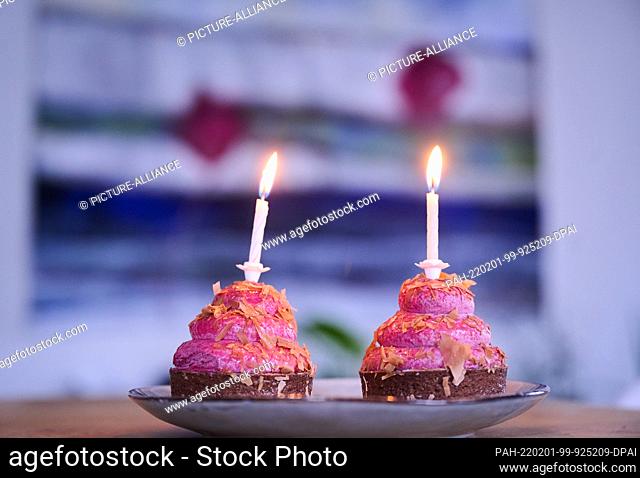 PRODUCTION - 12 January 2022, Berlin: ILLUSTRATION - Two cupcakes with burning candles stand on a table. (posed scene) The ""2"": symbol for opposites