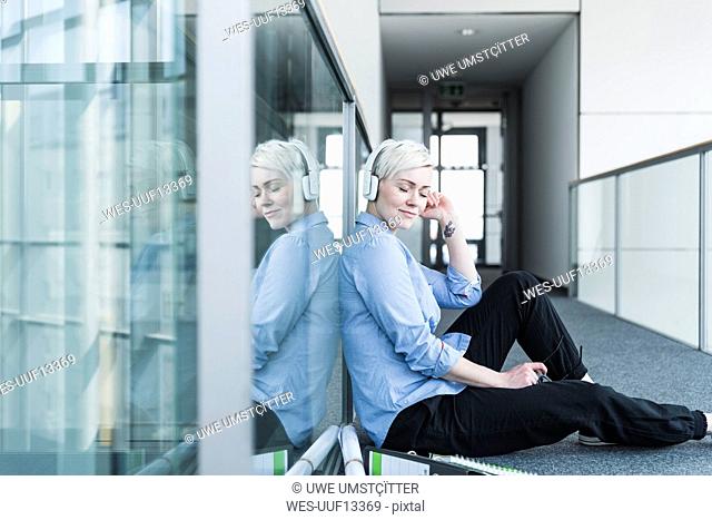 Woman sitting on office floor listening to music with headphones