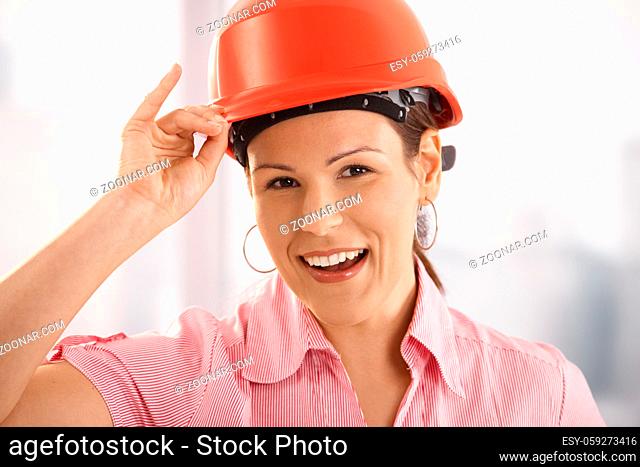 Happy young architect adjusting her hardhat, looking at camera, smiling