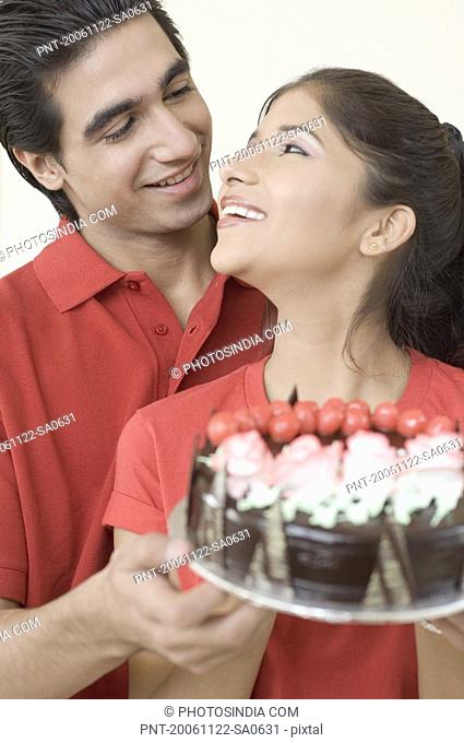 Close-up of a young couple holding a chocolate cake and looking at each other