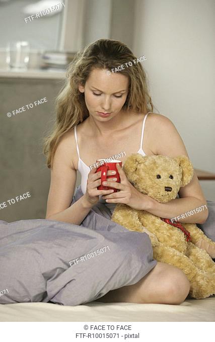 A blonde woman looking at the mug as she holds a teddy bear in her hand