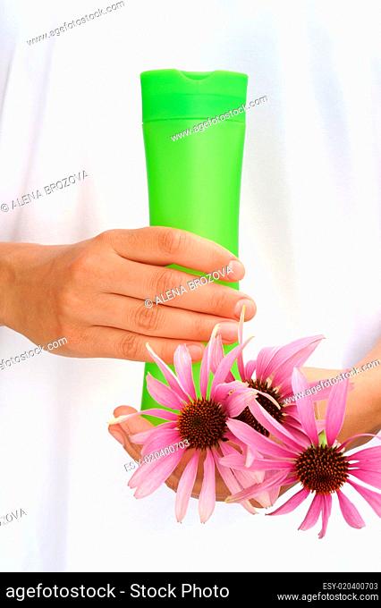 Hands of young woman holding cosmetics bottle and fresh coneflowers