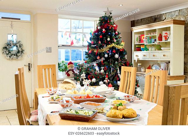 Empty dining room at Christmas time. It is decorated with a tree and other Christmas decorations. There is a selection of chinese food laid out on the dining...