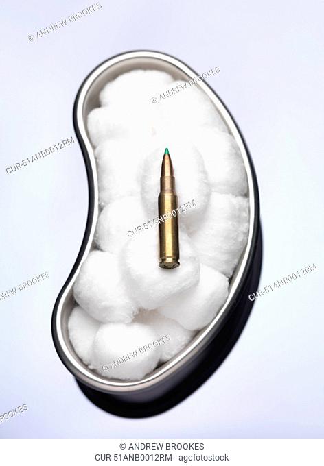 Bullet laying in cotton wool in surgical tray illustrating peace and diplomacy. Danger, bullet, weapons, crime