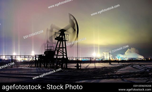 Oil and gas industry. Panoramic of a pumpjack on a oilfield and oil refinery on the winter sky background with light pillar effect . Night view