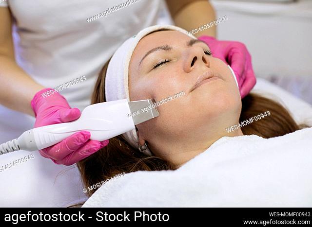 Woman taking ultrasonic facial treatment in salon