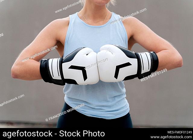 Sportswoman wearing boxing glove standing against wall
