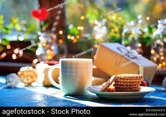Teacup and Christmas gluten free cookies on a table near the decorated window with gift boxes