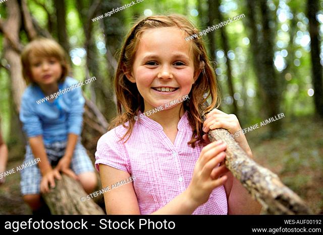 Portrait of smiling girl carrying log in forest