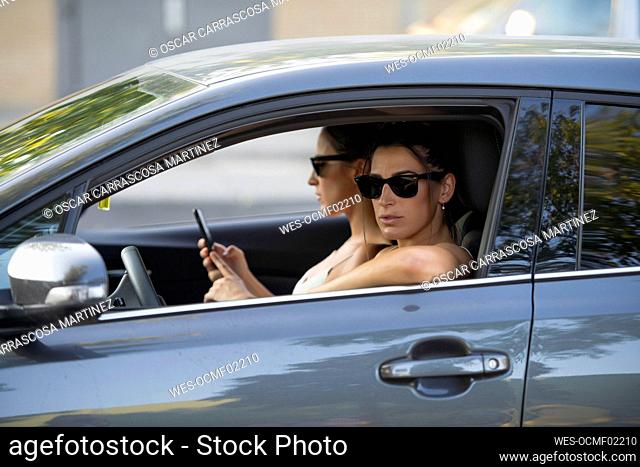 Woman looking through window while twin sister using smart phone in car