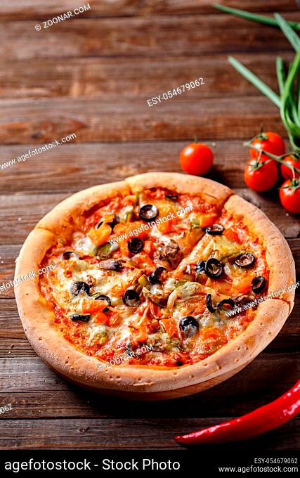 Pizza with tomato, mushroom and olives on wooden table with tomatos, fresh onion on background