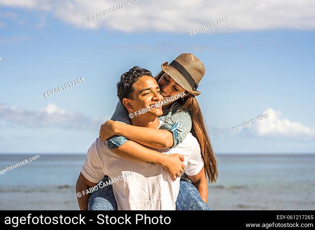 Young couple in love enjoy happiness and leisure activity - man carry woman in piggyback and smile with joyful - ocean water and blue sky in background -...