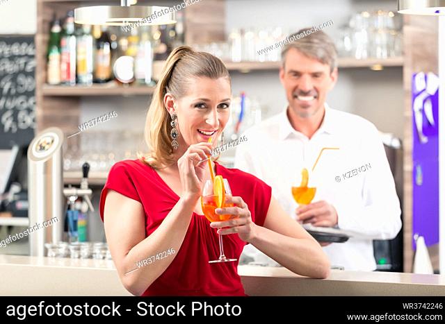 Happy woman drinking orange cocktail standing near bar counter