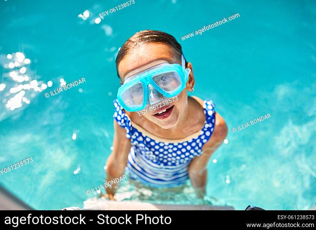 A child in goggles on the steps climbing out of the pool, little girl having fun in the swimming pool, summer vacation at home, tropical holiday resort