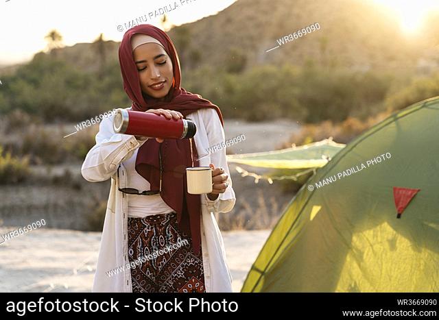 Smiling young tourist woman wearing Hijab at a tent pouring tea into mug