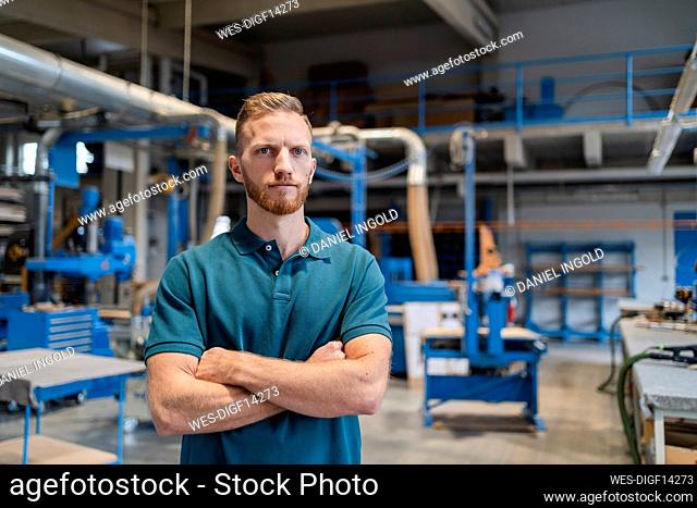 Portrait of carpenter posing in production hall with crossed arms