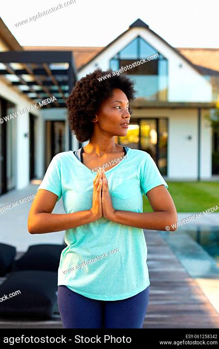 African american young woman practicing yoga and meditating near the pool