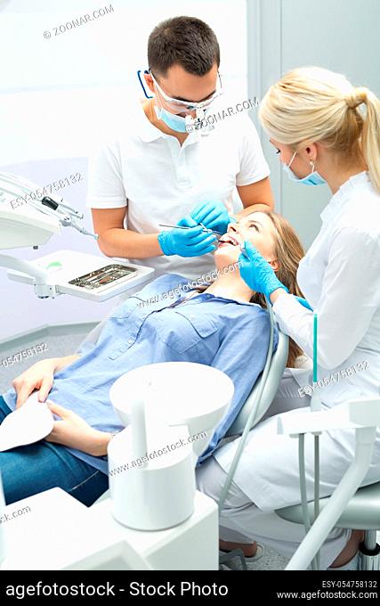 Young dentist working with the patient in a modern hospital. He is assisted by a young girl assistant. Doctor shows the example of the articulator of the human...