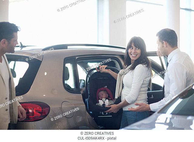Mid adult couple with baby girl trying out baby seat in car dealership
