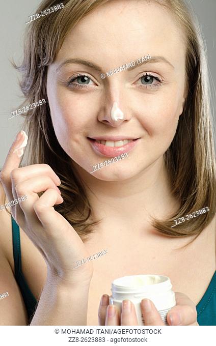 Attractive young woman applying moisturizing cream on her face